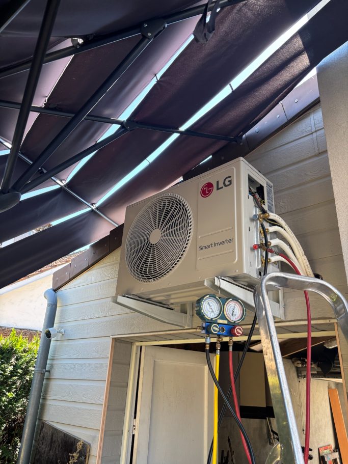 Installation d'un climatiseur extérieur Une unité extérieure de climatisation installé en hauteur, avec tuyaux et câbles apparents sous une toiture métallique.